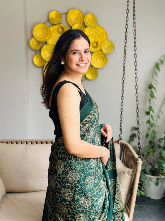 Woman in a green saree standing in a room with decorative wall art and plants.