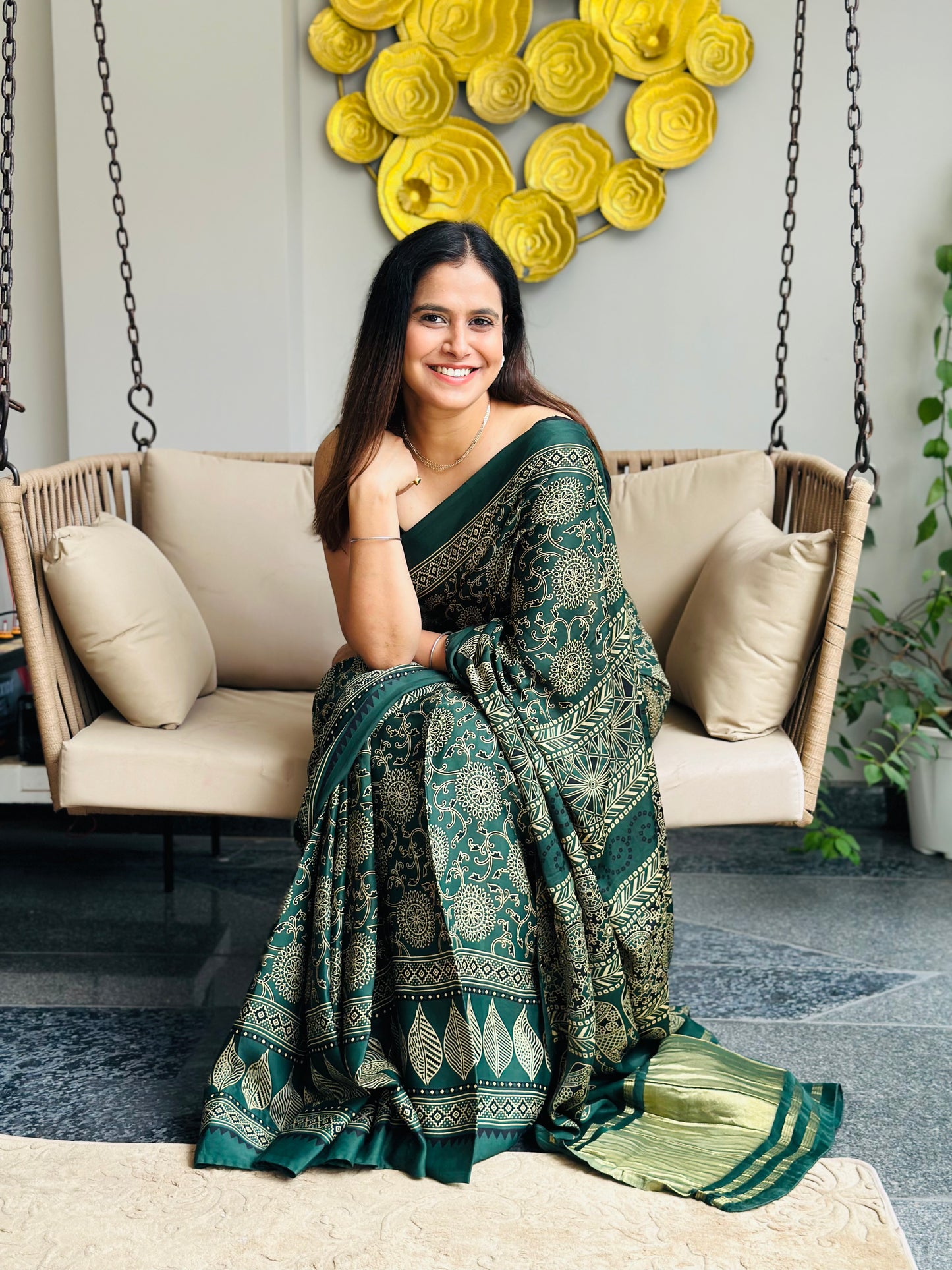 Woman in a green saree sitting on a swing in a decorated room.