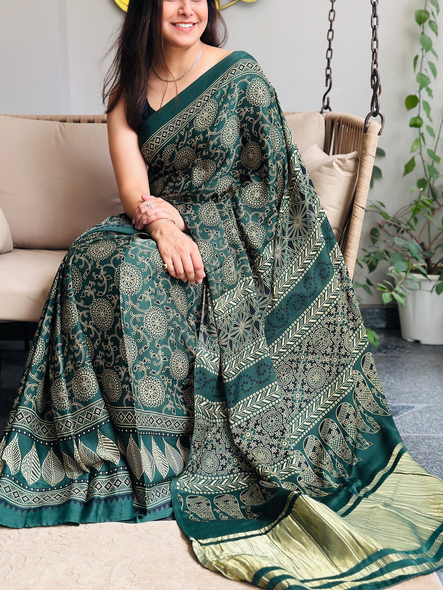 Woman wearing a green patterned saree sitting on a beige chair.